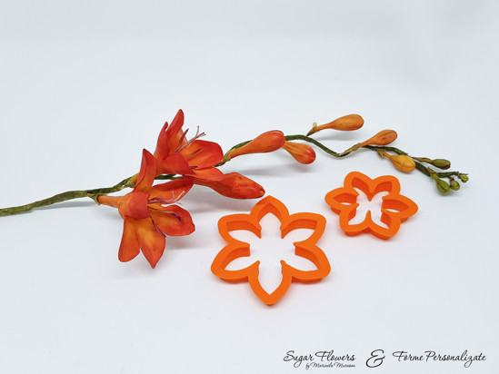 Decupatoare portocalii asezate pe masa langa o Frezie portocalie