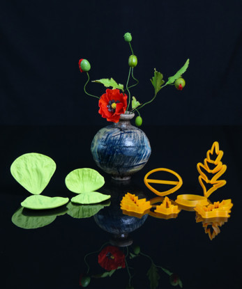 Veinere si decupatoare pentru mac, asezate in fata unei flori de mac, pe fundal negru.