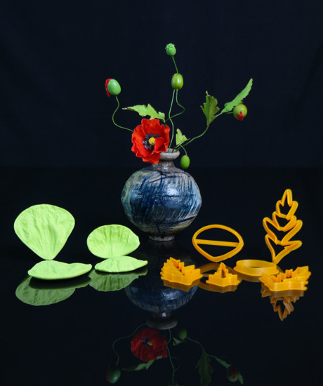 Veinere si decupatoare pentru mac, asezate in fata unei flori de mac, pe fundal negru.