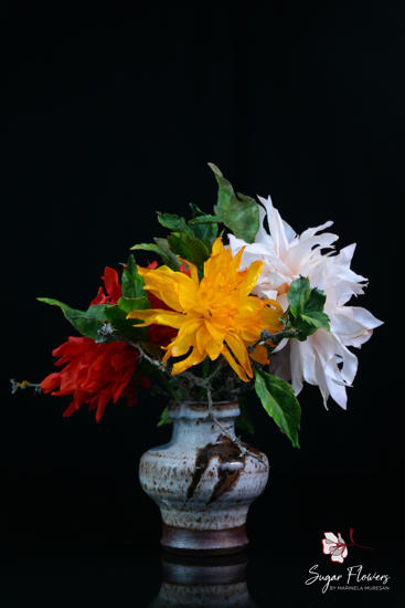 Vază ceramică artizanală cu un buchet spectaculos de dalii realizate din vafă în culorile roșu aprins, galben și alb, cu frunze verzi pe fundal negru