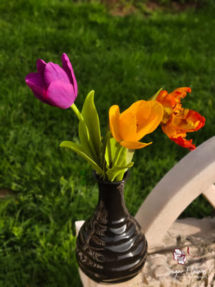 Lalele colorate in vaza neagra pe fundal natural verde